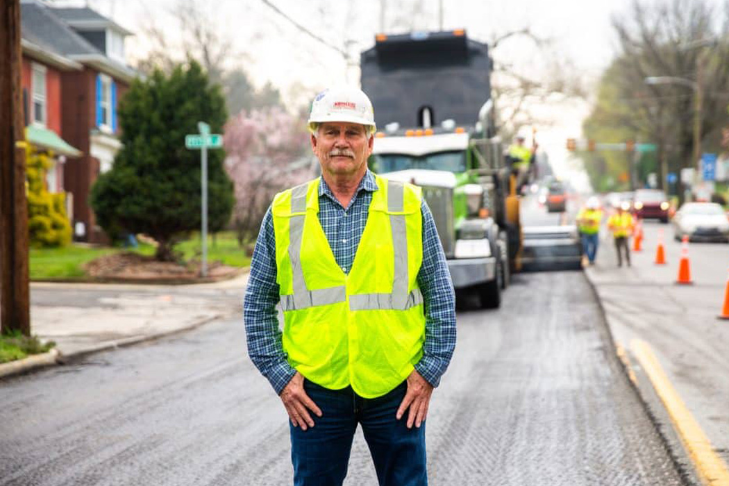 Headshot of a man on the paving crew with a plaid button up shirt, high visibility vest, and a hard hat.