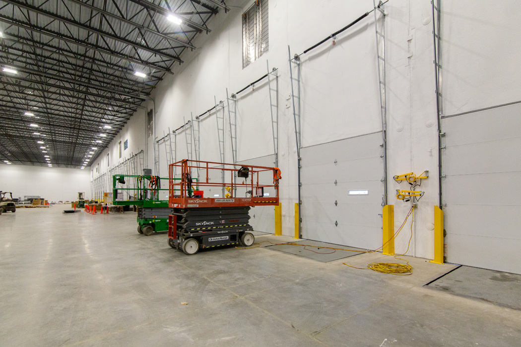 Warehouse interior with a countless amount of garage doors and orange and green man lifts.