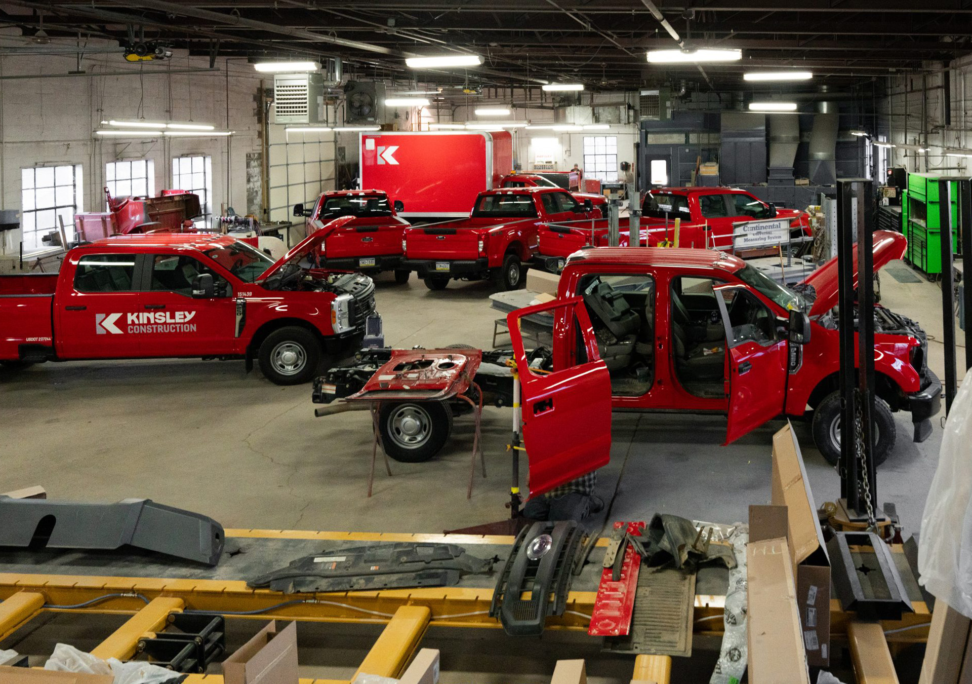 kinsley-constructions-truck-shop-hero-image Equipment repair shop with red trucks being repaired. Windows are on either side of the room and a garage door is on the left side of the room.
