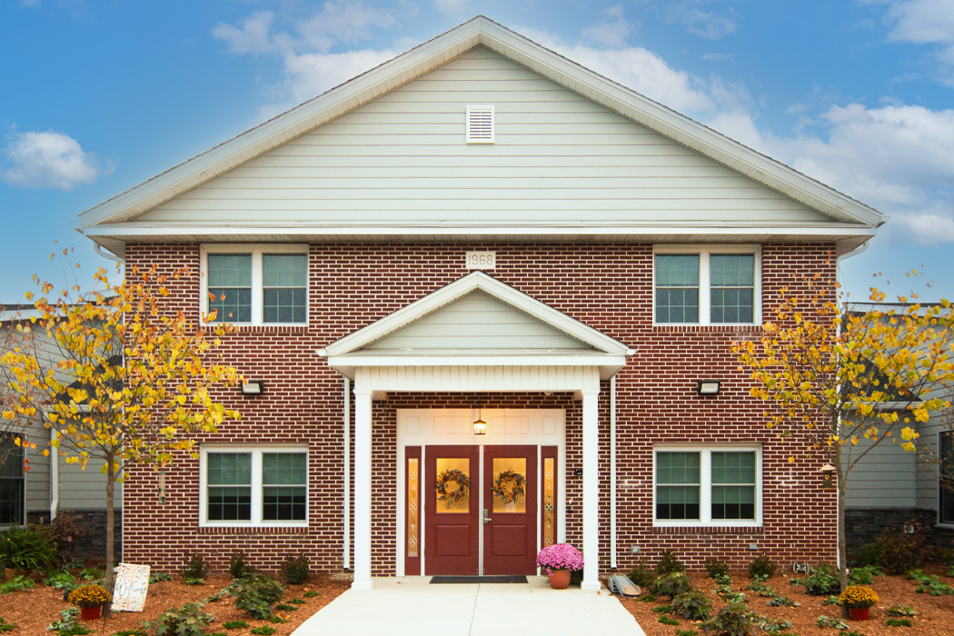 Red brick building with a red front door and trees and shrubs in front of the building.