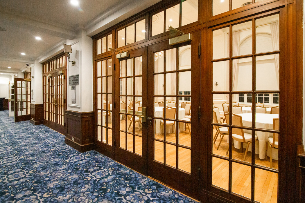 Looking into a dining room through medium-brown wood and glass lattice doors, you can see white circular tables and matching white chairs.