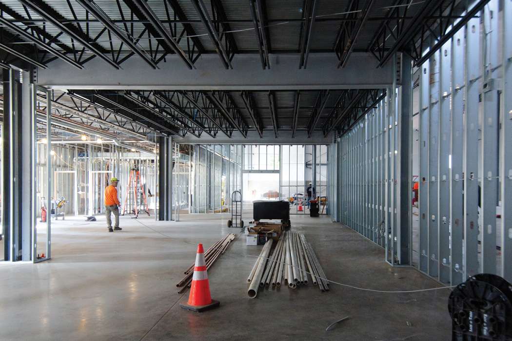 An empty commercial building under construction shows exposed metal framing and a lone worker.
