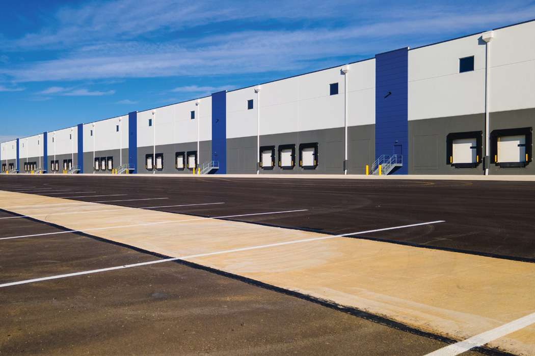 Blue, white, and grey warehouse exterior with a freshly paved black parking lot and white lines for parking spots