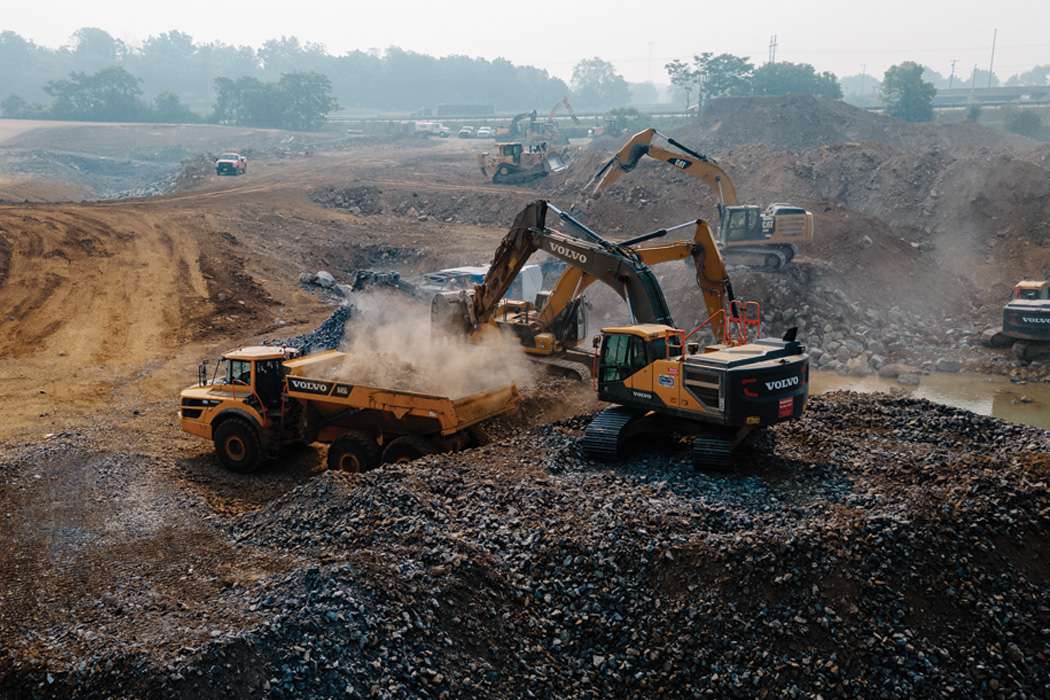Two yellow excavators dumping materials into a large construction vehicle