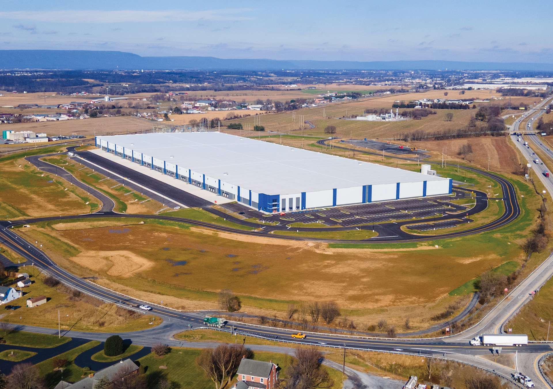 alleman-road-site-work-hero Aerial view of a large white and blue warehouse that is next to a highway