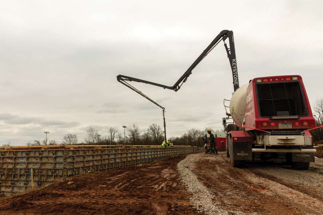 A concrete pump truck pours cement into a large form.