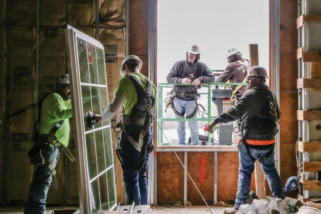 Five men wearing safety equipment installing a window