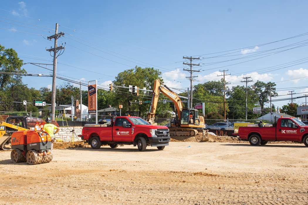 Construction workers and equipment are at a site under a sunny sky.