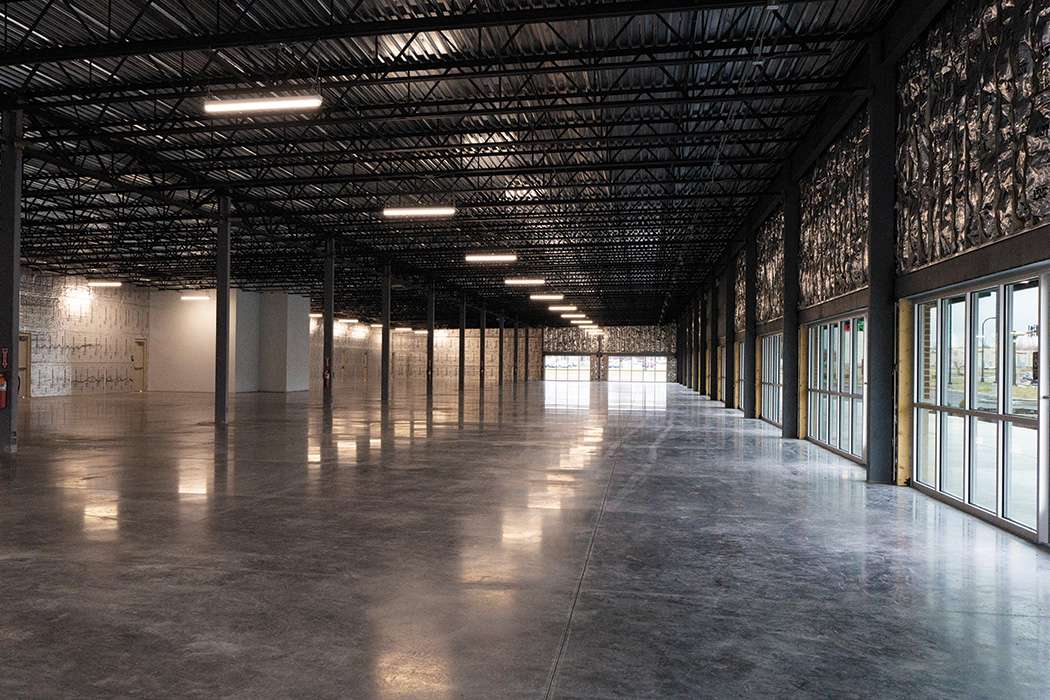Empty interior of a building with a polished concrete floor, steel support beams, and large windows.