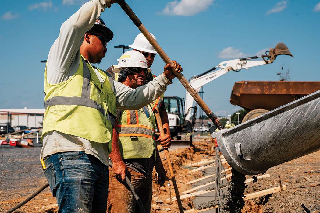 Two men in neon vests working with concrete coming out of a concrete mixing truck