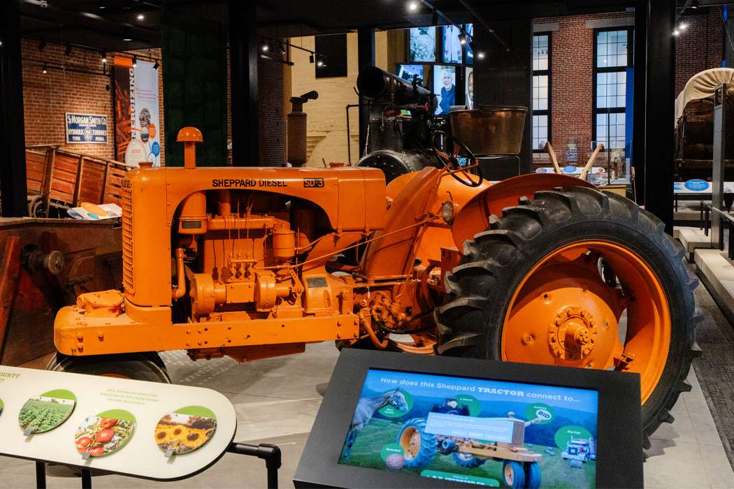 An orange antique Shepard tractor is displayed in a museum.