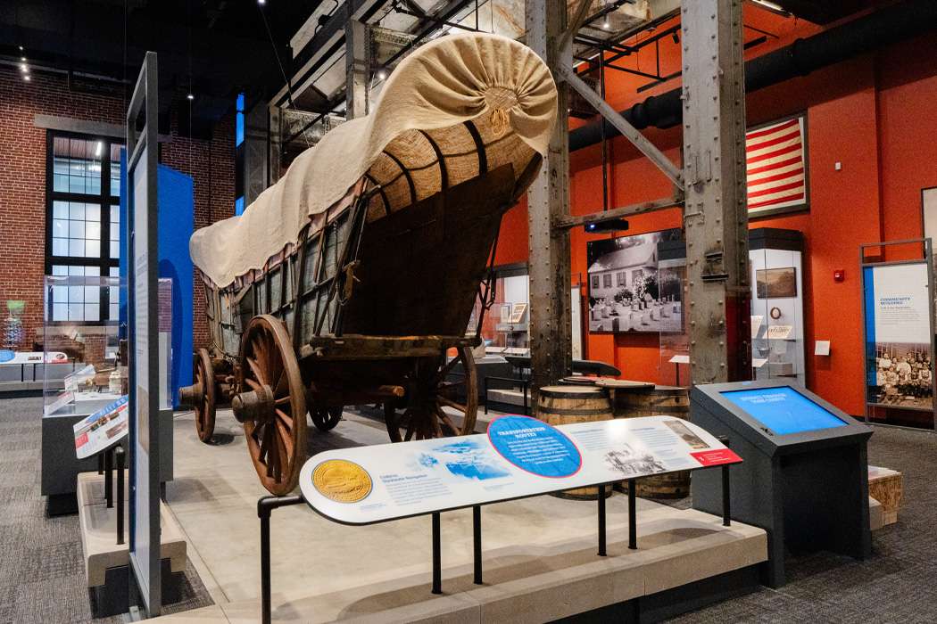 A large, covered wagon is the centerpiece of a museum exhibit.
