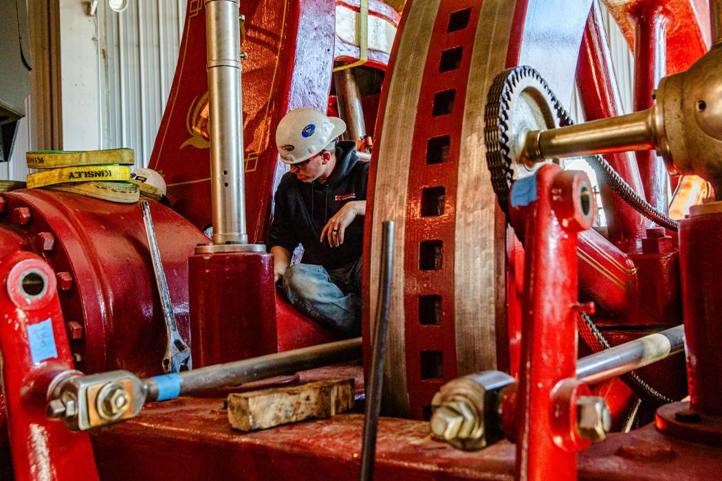 A worker in a hard hat repairs large red industrial machinery.