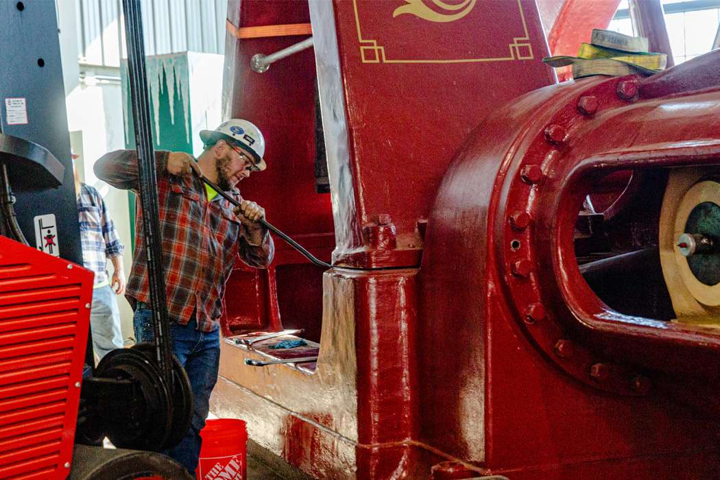 A worker uses a long bar to adjust a large red machine.