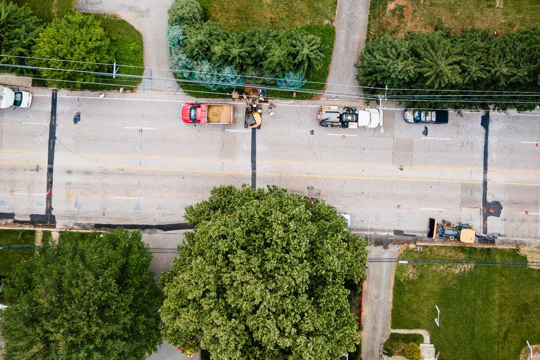 Roadwork in progress on a residential street surrounded by lush trees.