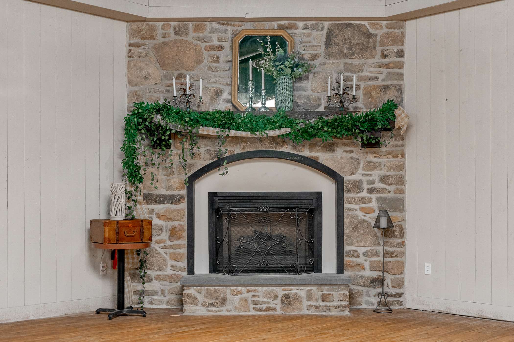 A rustic stone fireplace with a garland and candles sits against a wood floor.