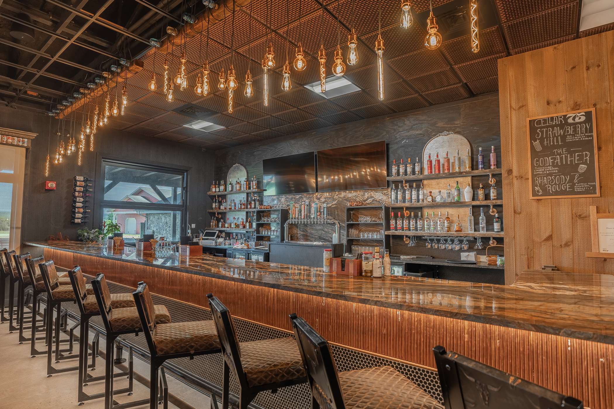 A long, wood-topped bar with numerous stools and shelves stocked with bottles.