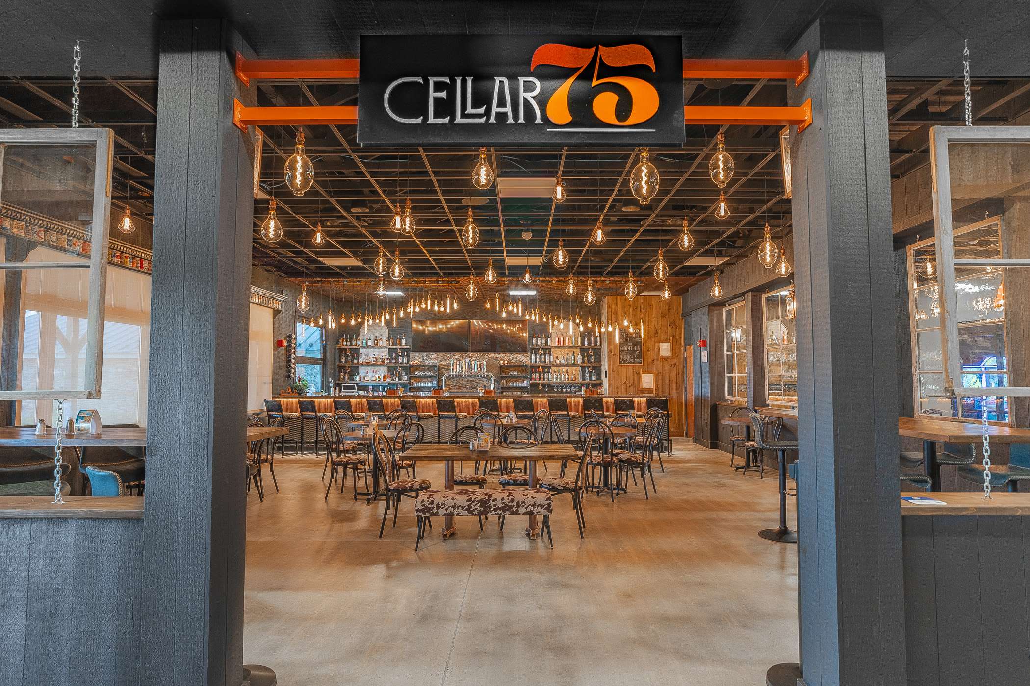 The interior of Cellar 76 restaurant is shown, featuring a rustic-industrial design with exposed ceilings and warm lighting.