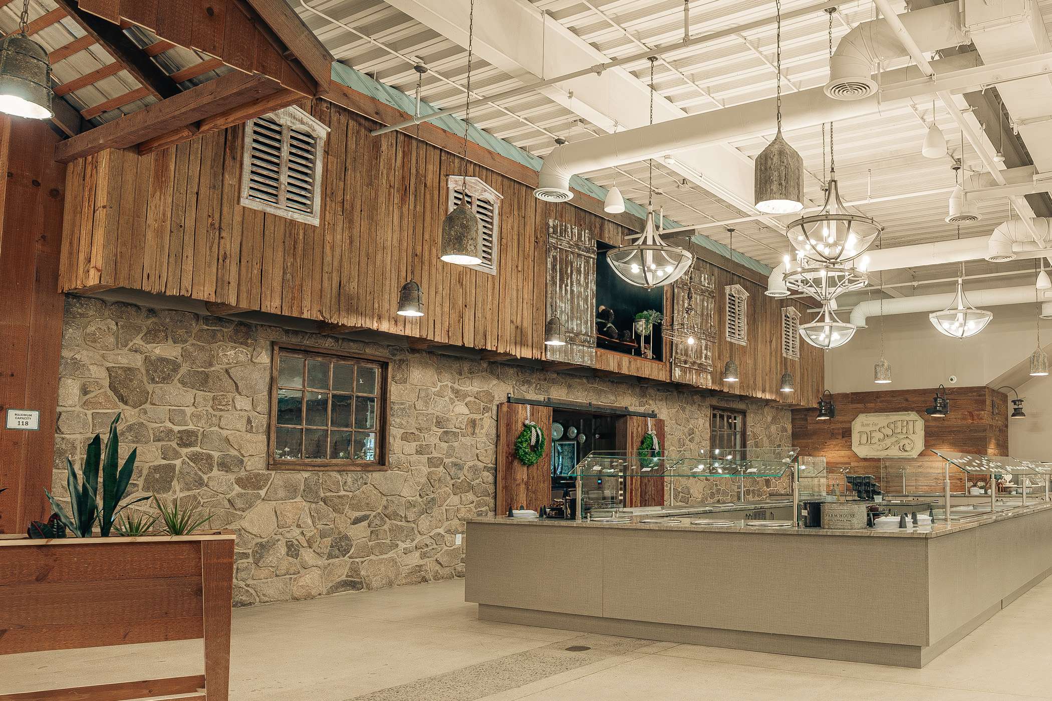 A rustic-chic interior with exposed wood and stone walls, a high ceiling, and modern lighting fixtures.