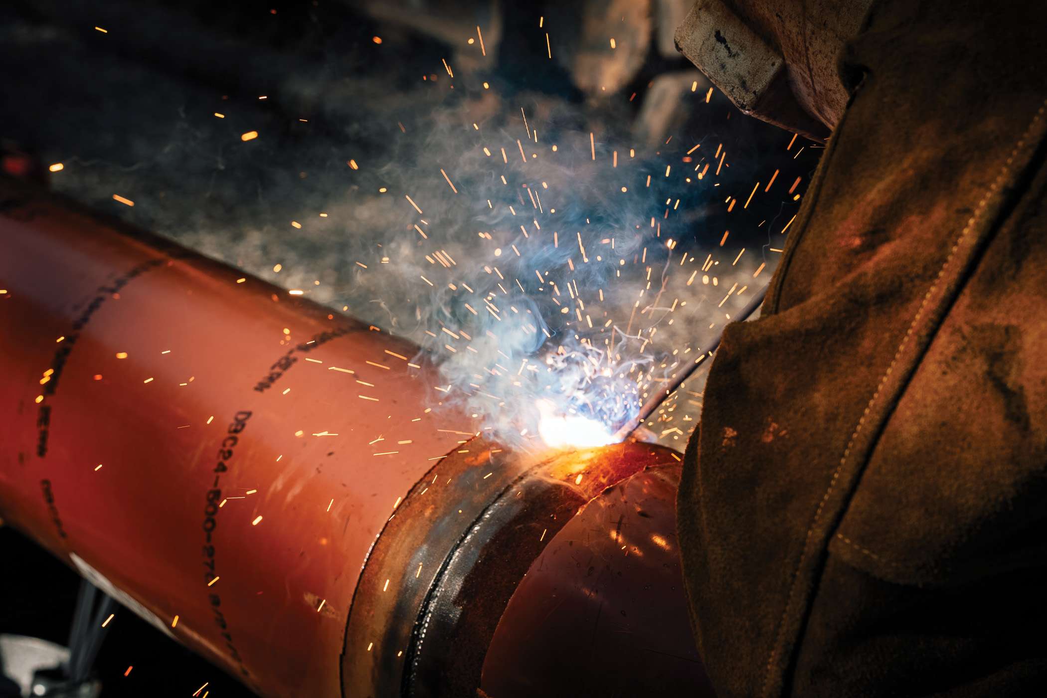 Man in protective gear is welding a pipe with a torch in a tent.