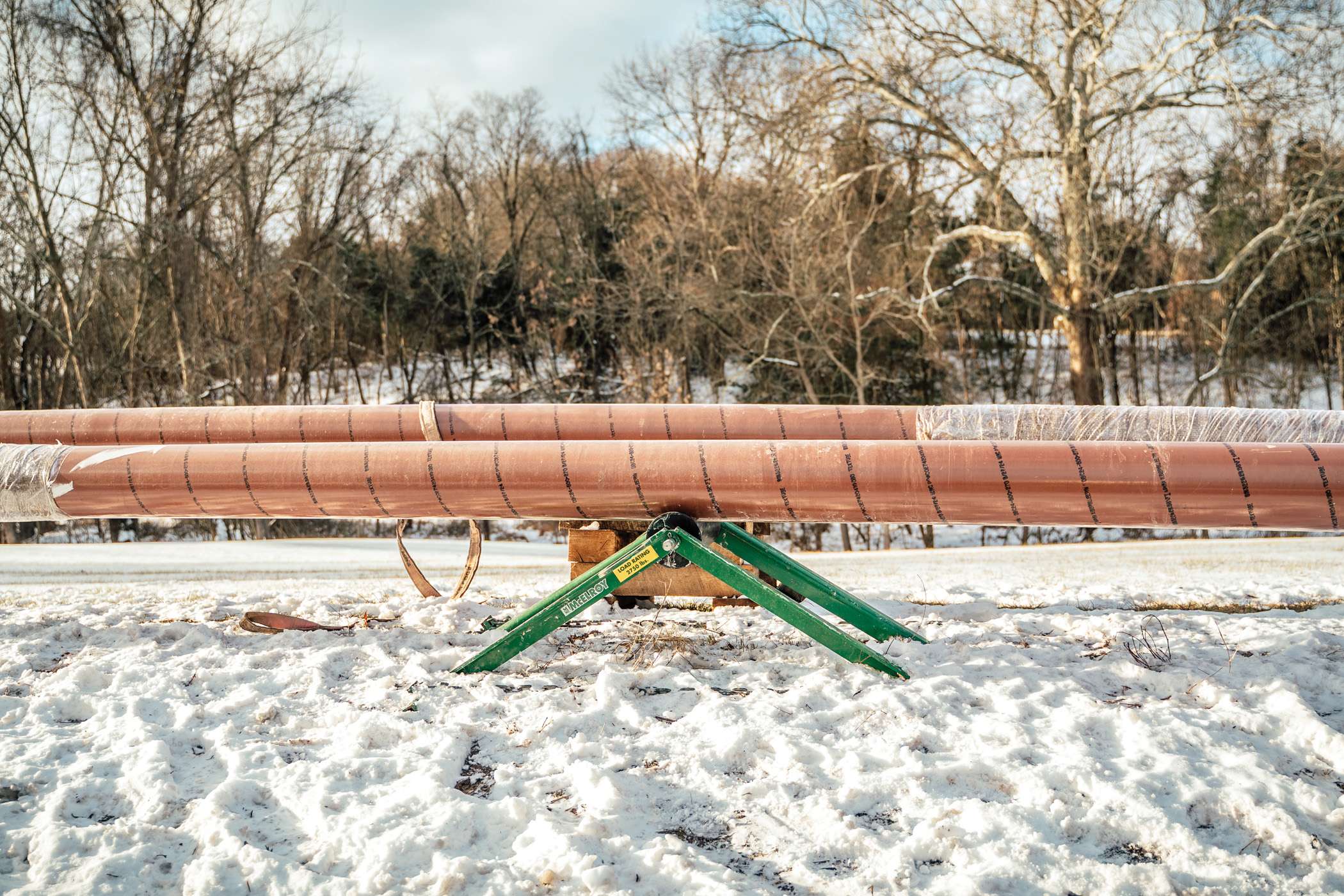 Large pipes rest on a green metal stand in a snowy landscape.