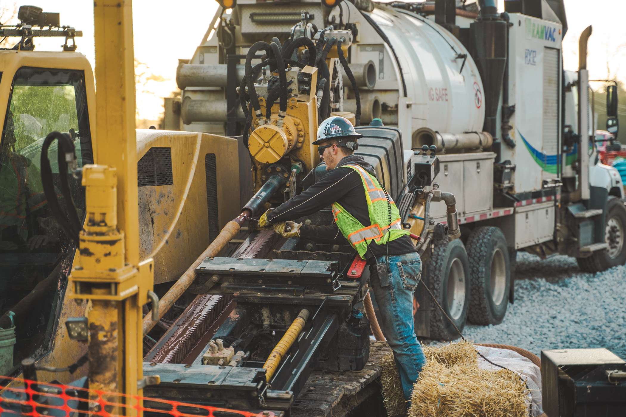 A worker operates drilling equipment attached to a large vacuum truck.