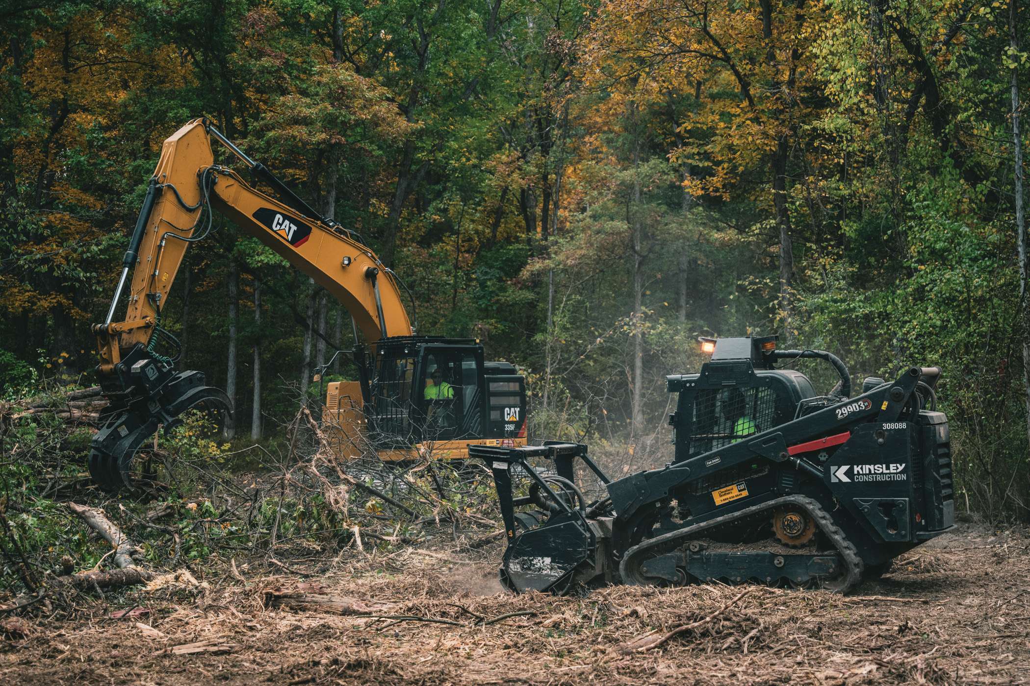 Heavy machinery clears trees and brush in a wooded area.