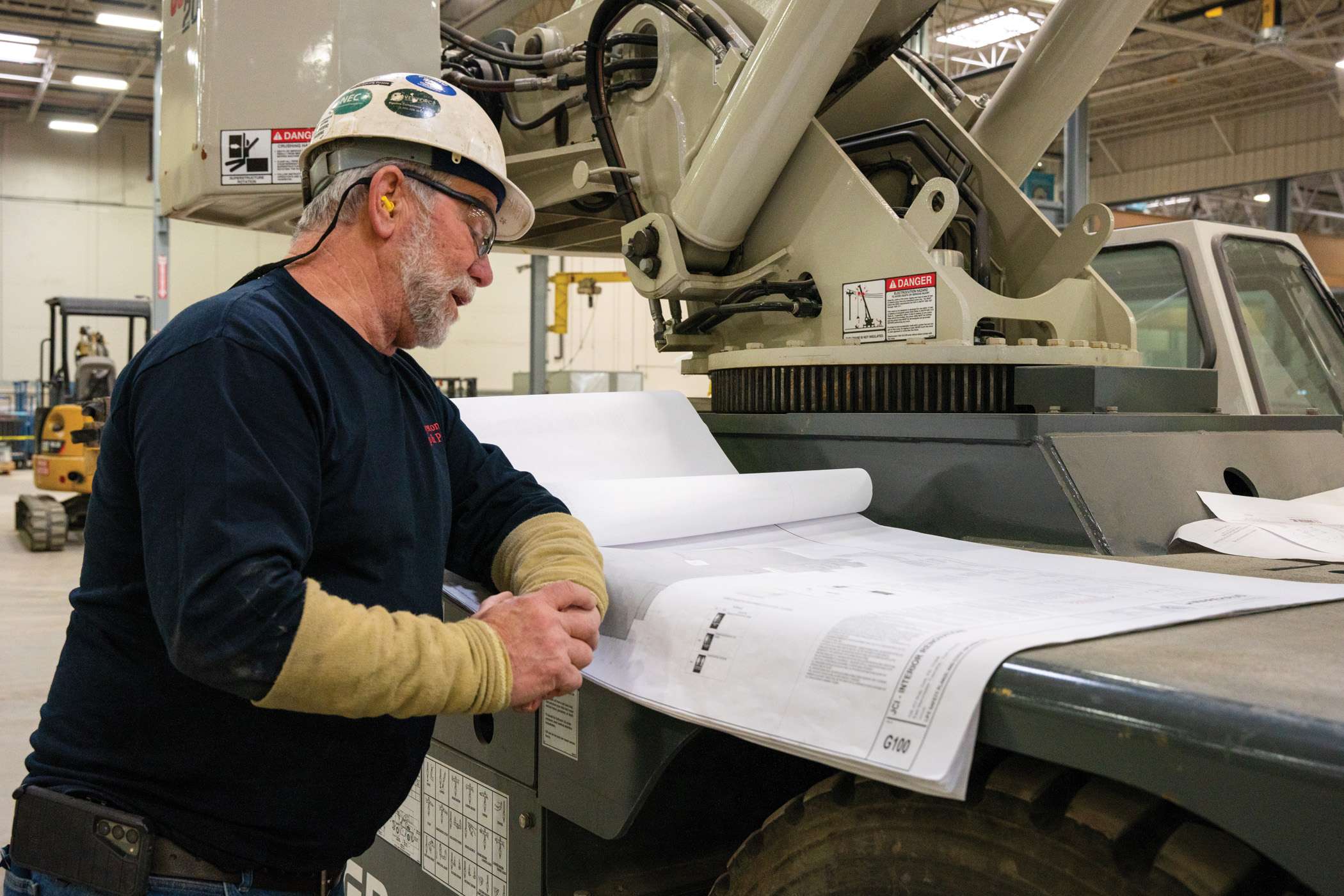 A construction worker reviews blueprints while standing next to a piece of heavy machinery.