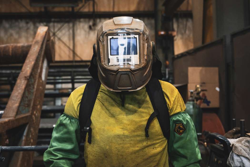 A person in safety welding gear stands in an industrial setting.