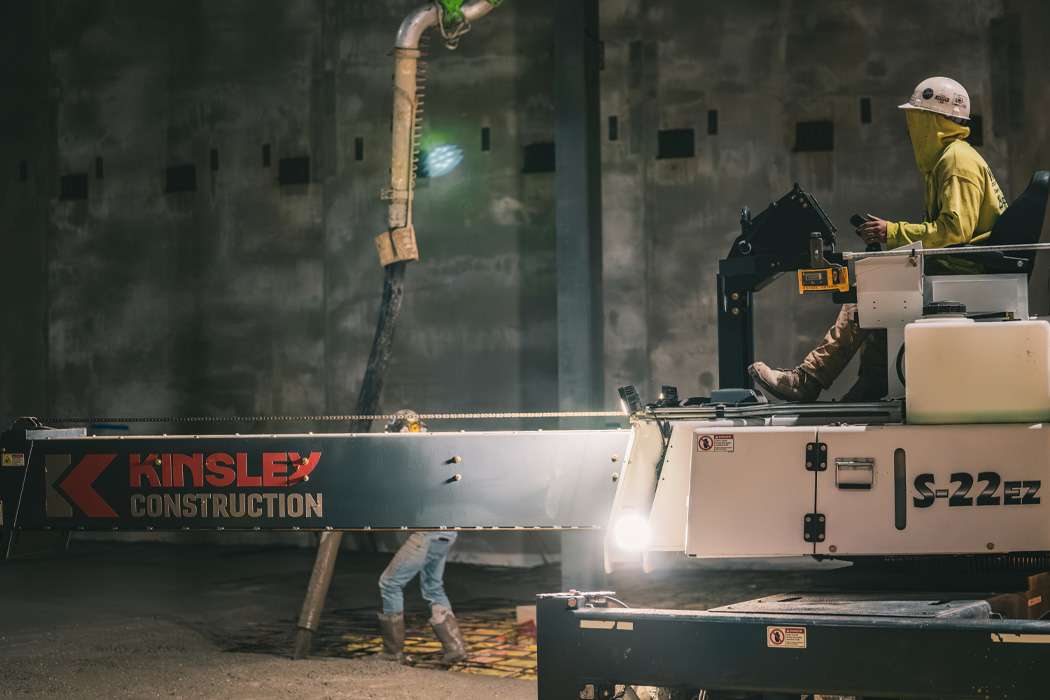 A construction worker operates a machine that appears to be spraying or applying material to a concrete structure.