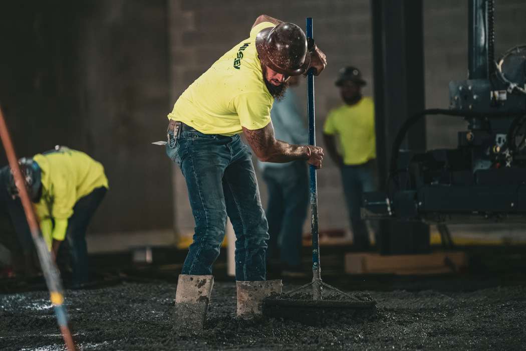 Construction workers in neon shirts and hard hats smooth out asphalt