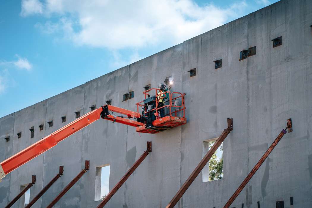 Construction workers use man lifts to attach braces to a large concrete wall.