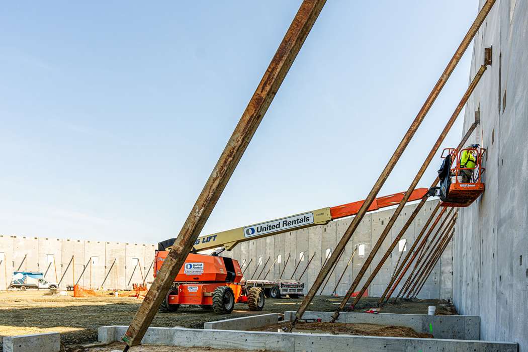 Construction workers use man lifts to attach braces to a large concrete wall.