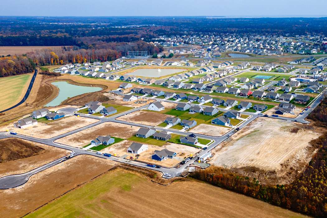 An aerial view shows a suburban development under construction interspersed with agricultural fields.