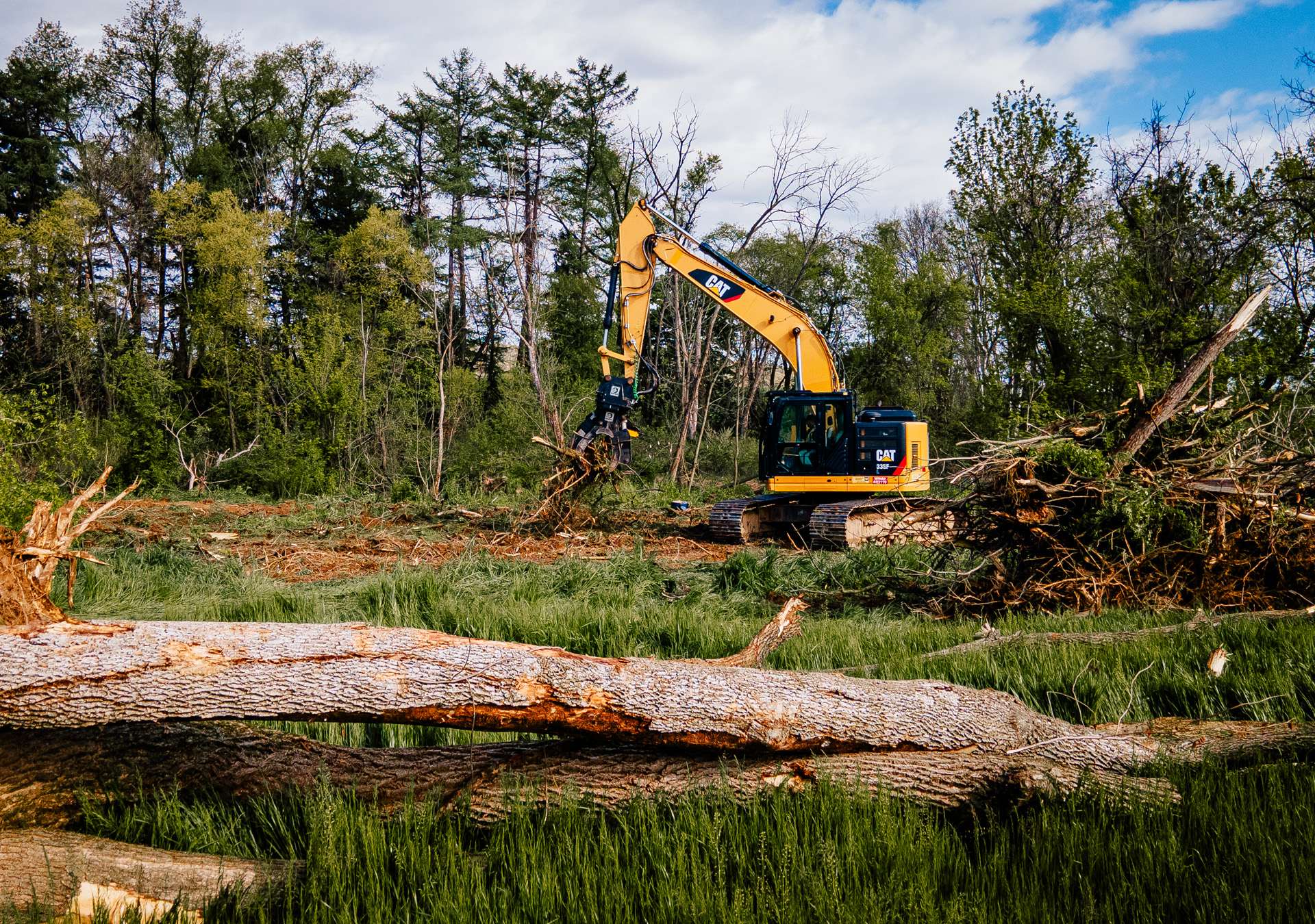 kinsley-clearing-crew-hero An excavator is clearing trees in a wooded area, with logs in the foreground.