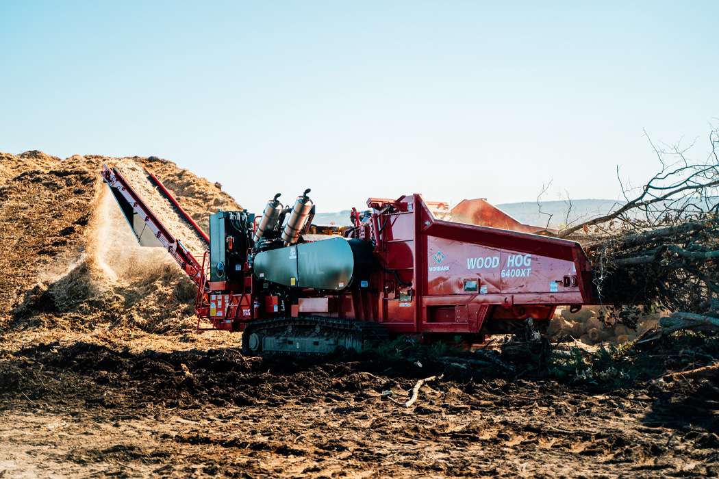A red "Wood Hog 6400XT" machine grinds wood into mulch.