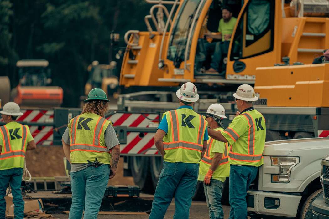 Construction workers in safety vests standing near yellow construction equipment