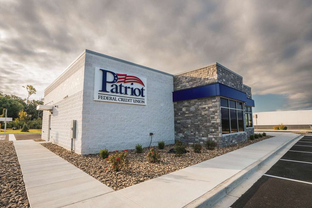 A white and grey stone building, with blue accents, and a parking lot
